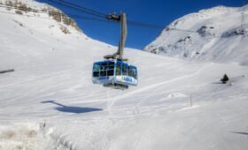 Skier on a groomed run at Lake Louise Ski Resort in the Canadian Rockies, Alberta, with snow-covered mountain peaks and blue sky in the background