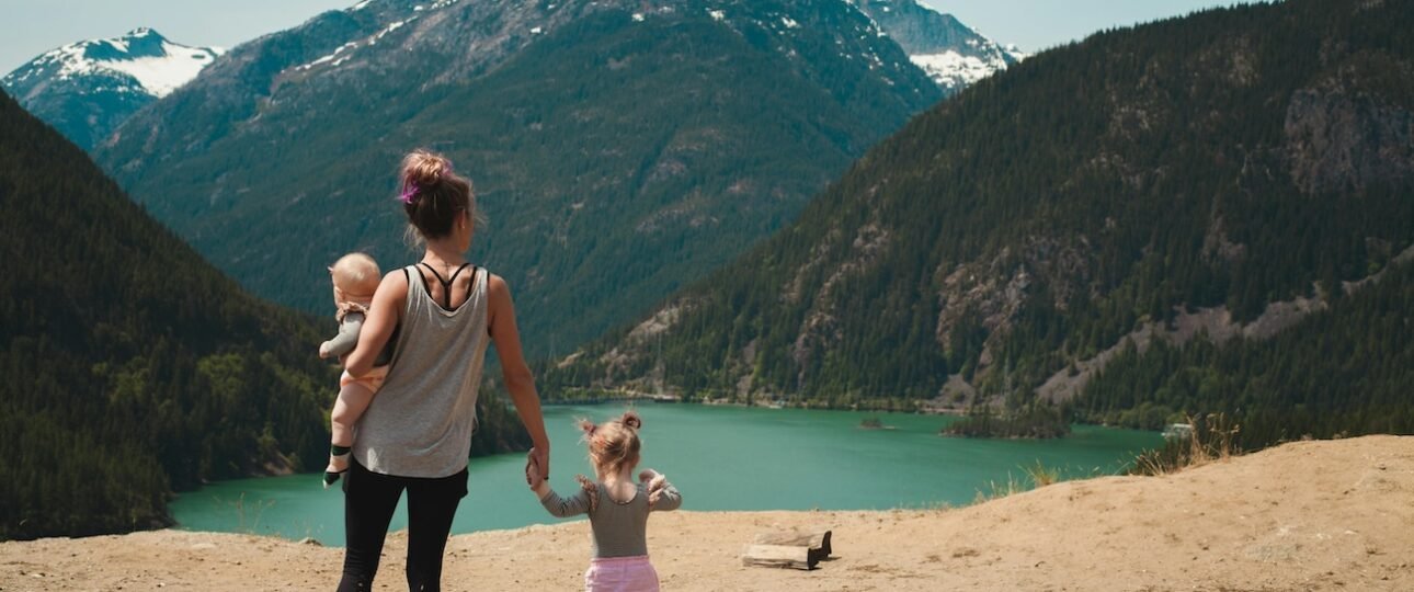 A family with young children hiking a mountain trail in Banff National Park, Alberta, with turquoise glacial lake and Rocky Mountain peaks in the background