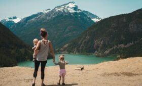 A family with young children hiking a mountain trail in Banff National Park, Alberta, with turquoise glacial lake and Rocky Mountain peaks in the background