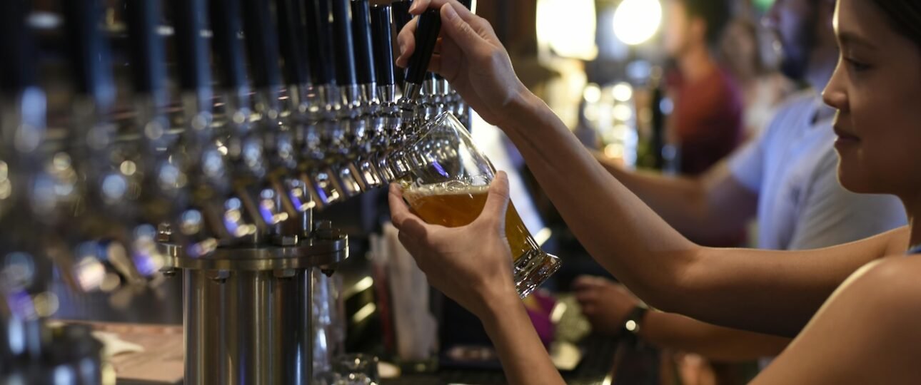 Two craft beer pints on a wooden table on a brewery patio with Canadian Rocky Mountain peaks visible in the background, Canmore, Alberta