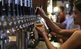 Two craft beer pints on a wooden table on a brewery patio with Canadian Rocky Mountain peaks visible in the background, Canmore, Alberta