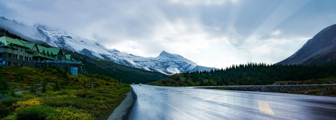 Empty two-lane road stretching toward snow-capped mountain peaks on the Icefields Parkway, Banff National Park, Alberta, Canada
