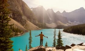 Hiker standing at Sentinel Pass above Larch Valley with golden larch trees, turquoise Moraine Lake, and the Valley of Ten Peaks in the background, Banff National Park, Alberta