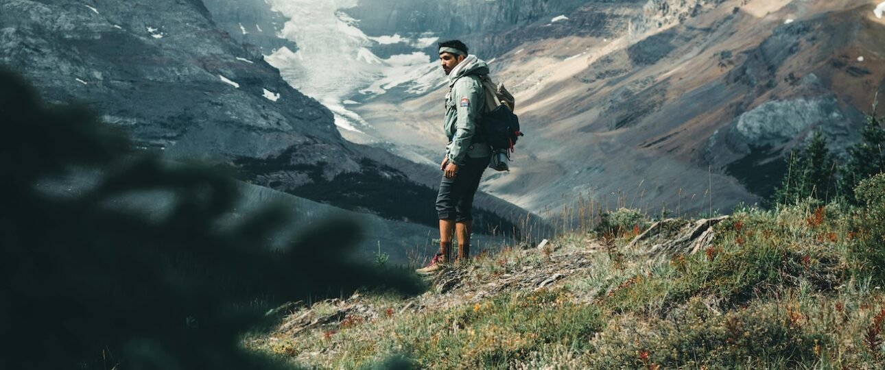 A hiker on a trail surrounded by golden larch trees in Larch Valley above Lake Louise in autumn, with snow-capped peaks in the background, Banff National Park, Alberta, Canada