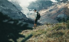 A hiker on a trail surrounded by golden larch trees in Larch Valley above Lake Louise in autumn, with snow-capped peaks in the background, Banff National Park, Alberta, Canada