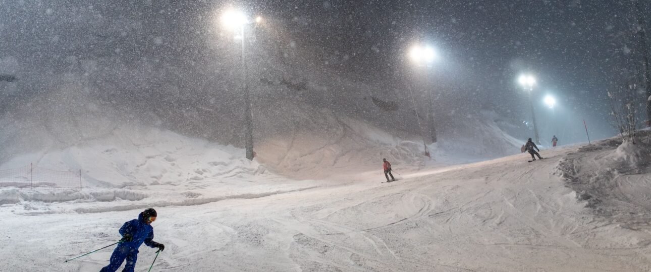 Skiers on a floodlit run at Kinosoo Ridge night skiing near Cold Lake, with the chairlift and chalet lights below.