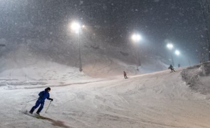 Skiers on a floodlit run at Kinosoo Ridge night skiing near Cold Lake, with the chairlift and chalet lights below.